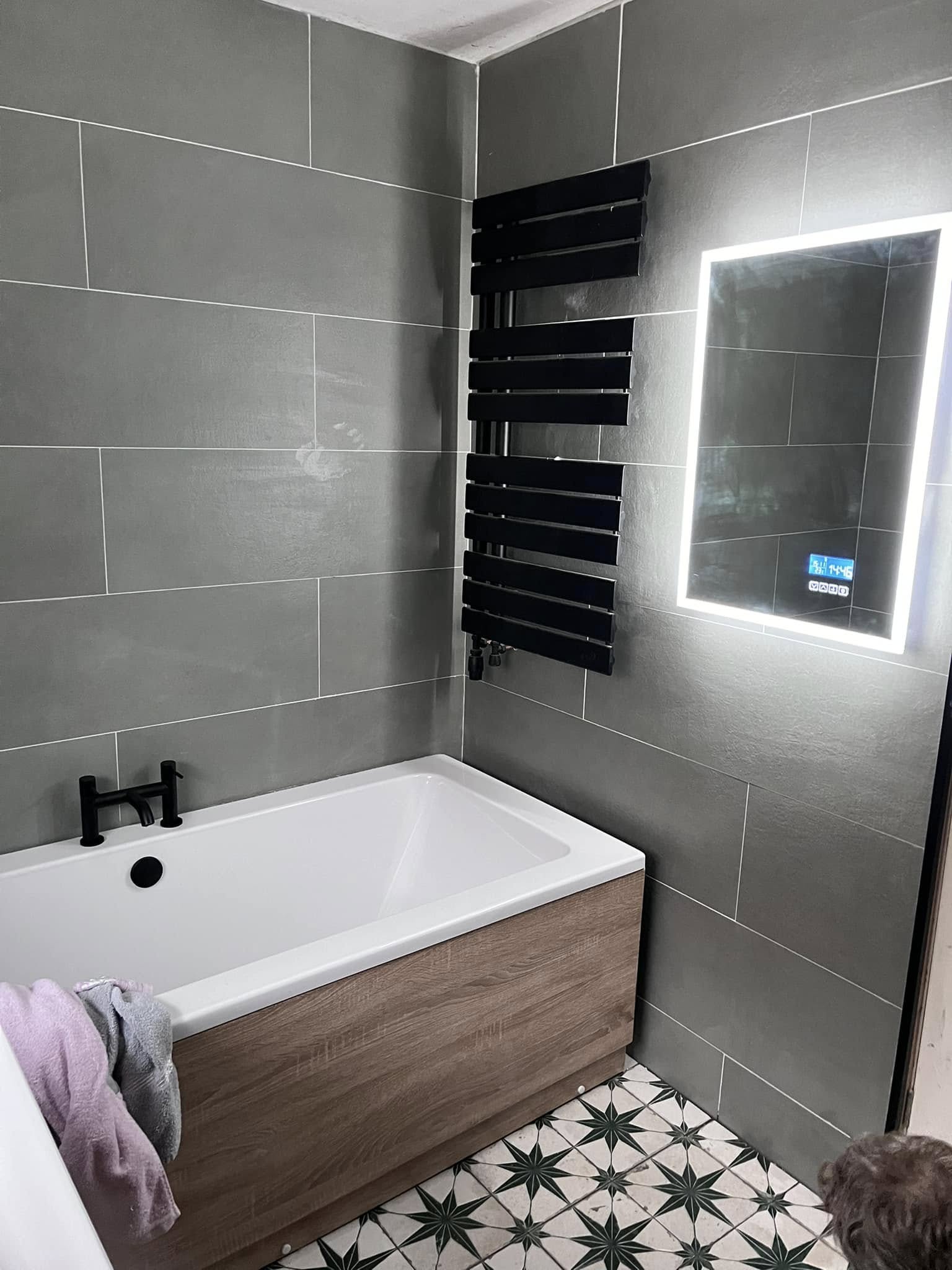 Grey-tiled bathroom with black towel rail